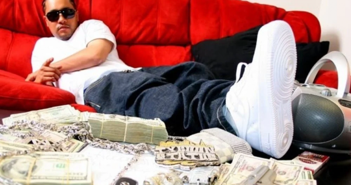 说唱歌手在沙发上摆拍 桌面有现金与配饰的宣传照（与案件报道相关的示意图）