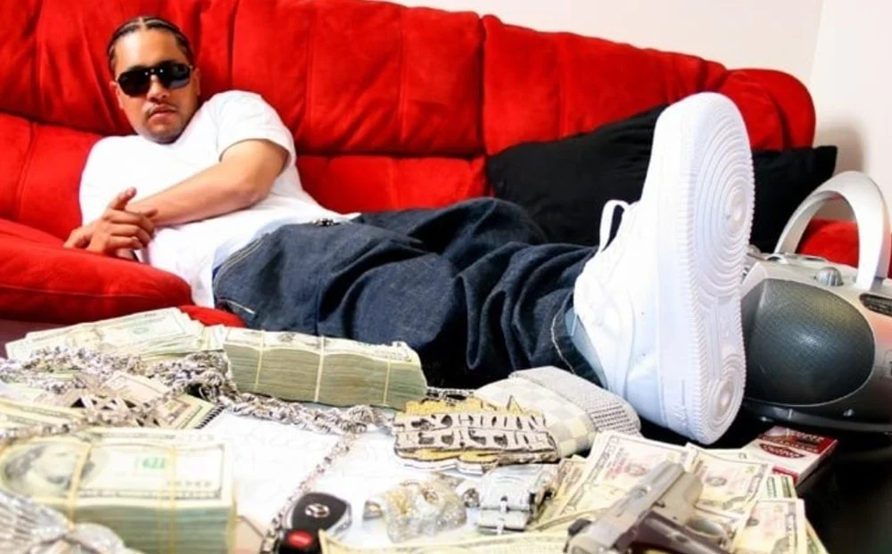 说唱歌手在沙发上摆拍 桌面有现金与配饰的宣传照（与案件报道相关的示意图）