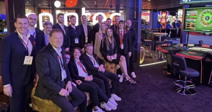 Spintec 团队在国际游戏展会合影，背景为电子赌枱与自动轮盘展位