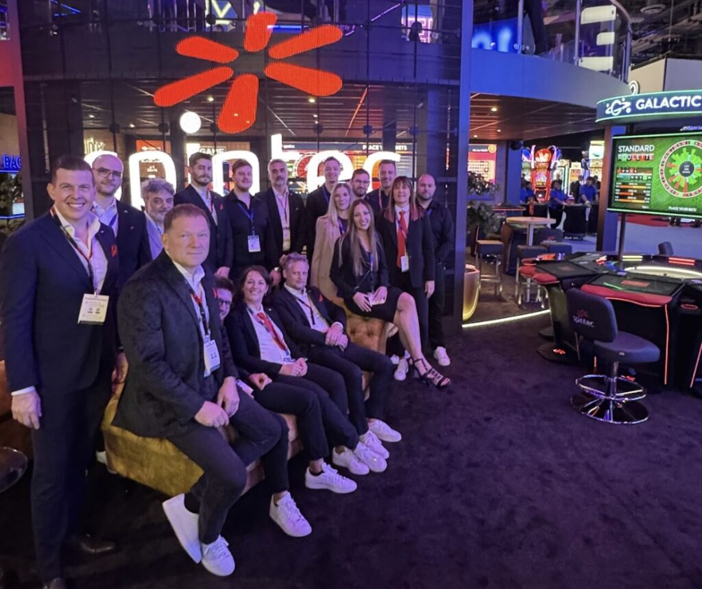 Spintec 团队在国际游戏展会合影，背景为电子赌枱与自动轮盘展位