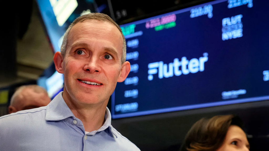 Flutter Entertainment（颤振娱乐）首席执行官彼得·杰克逊（Peter Jackson）在纽约证券交易所，背景可见Flutter标志。