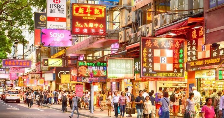 香港繁忙的街道上，行人如织，两侧林立着各式各样的霓虹灯商店招牌，展现独特的都市商业景观。