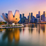新加坡滨海湾金沙和城市天际线黄昏景观。标志性的艺术科学博物馆（ArtScience Museum）矗立在水边，背景是金融区摩天大楼的倒影。图片展示了新加坡旅游业强劲复苏的活力，呼应 2025 年经济增长预期上调至 4%。