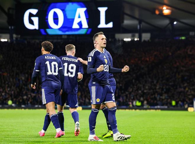 苏格兰球员在进球后握拳怒吼庆祝，身后大屏幕显示进球字样的比赛画面