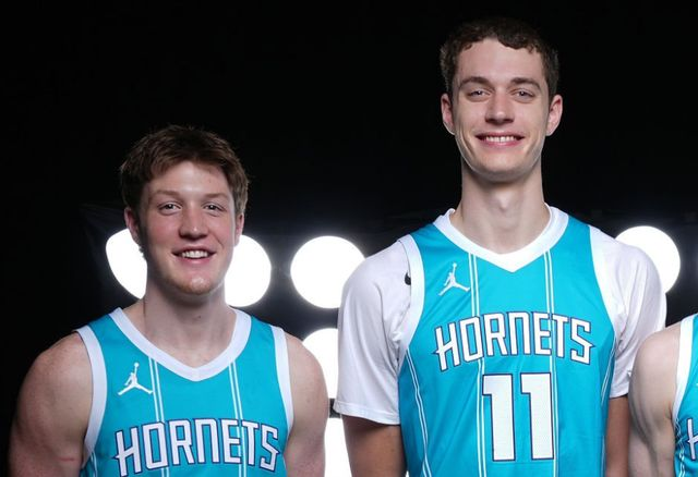 两名身穿浅蓝球衣的黄蜂年轻内线球员在灯光前合影的照片