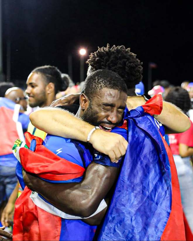 一名裹着国旗的海地球员激动落泪，与队友紧紧相拥的特写画面