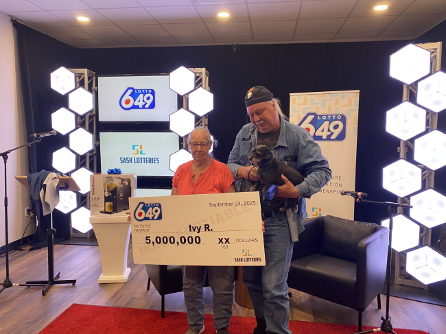 颁奖现场合影，中奖者手持巨额支票与友人及宠物狗合照，背景为Lotto 6/49与Sask Lotteries标识。
