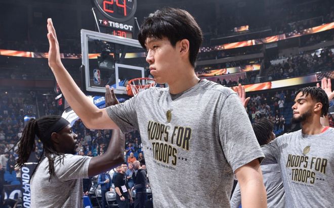 杨瀚森在赛前与队友击掌致意，身穿灰色热身T恤，背景为灯光明亮的球馆。