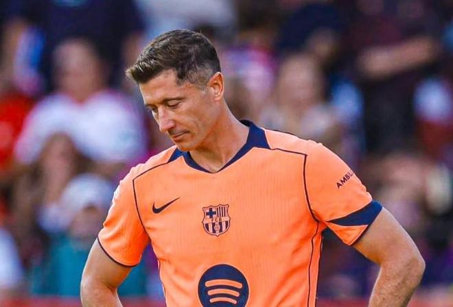 身穿橙色客场球衣的巴萨前锋莱万低头沉思的近景照，背景为模糊看台与观众。