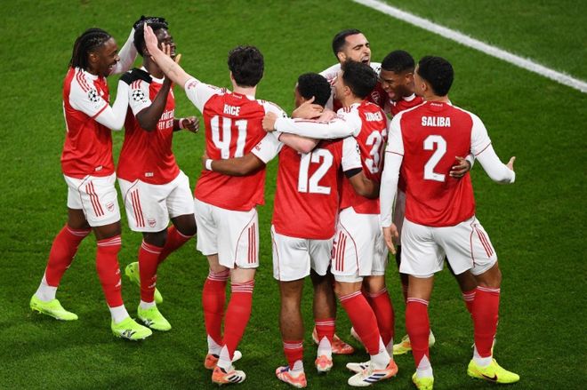 阿森纳队（红白球衣）球员在欧冠联赛中围在一起庆祝进球，体现了球队在 3-1 击败拜仁后高涨的士气和全胜领跑的强势地位。此图象征阿森纳在欧冠第 5 轮后强势晋级的良好势头。