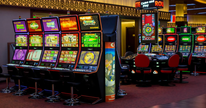 : 一排排灯光明亮的老虎机和电子赌桌，摆放在赌场内部，地面铺着红色地毯。