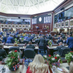 佛罗里达州议会大厅内，议员们正在进行立法会议的场景，背景显示数字屏幕，象征HB 591和HB 189法案的审议进程。