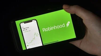 一张手持智能手机的照片，屏幕上显示着 Robinhood 交易应用程式的绿色标志和股票图表，代表其进入预测市场领域，对体育博彩构成竞争威胁。