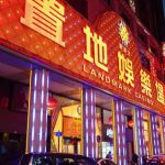 澳门置地广场赌场的夜景特写，建筑外墙有巨大的中文“置地娛樂場”霓虹灯招牌，夜间灯光璀璨，有多辆出租车停靠在入口处。