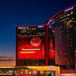 美國拉斯維加斯雲頂世界（Resorts World Las Vegas）度假村夜景，巨大的紅色曲面建築上顯示著數字內容和「Resorts World」標誌。