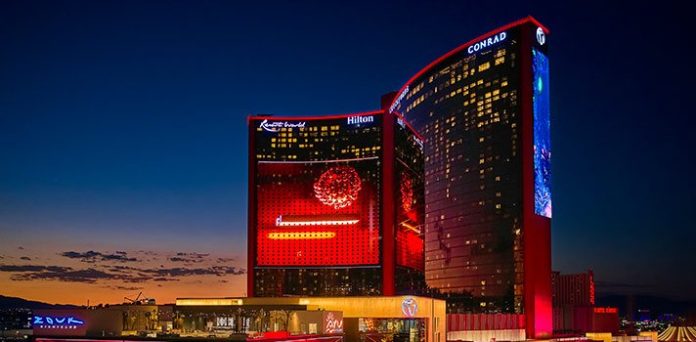 美國拉斯維加斯雲頂世界（Resorts World Las Vegas）度假村夜景，巨大的紅色曲面建築上顯示著數字內容和「Resorts World」標誌。