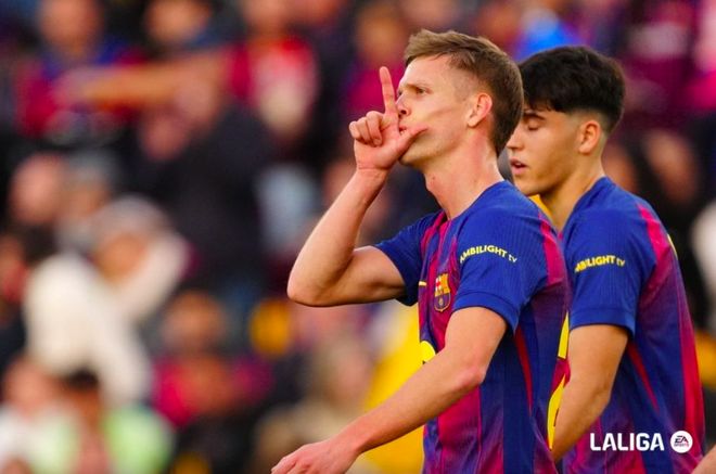 球員進球後在西甲比賽中慶祝，手指向天，身著巴薩主場球衣。