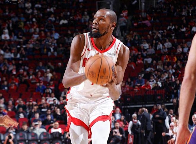 休斯顿火箭队超级巨星凯文·杜兰特（Kevin Durant）身穿白色球衣，在 NBA 比赛中持球进攻，周围是观众席背景。