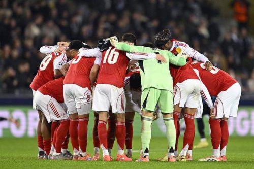 阿森納球員（紅白球衣）在足球場上進行賽前或中場的圓陣喊話，門將穿著螢光綠色球衣，體現團隊士氣。