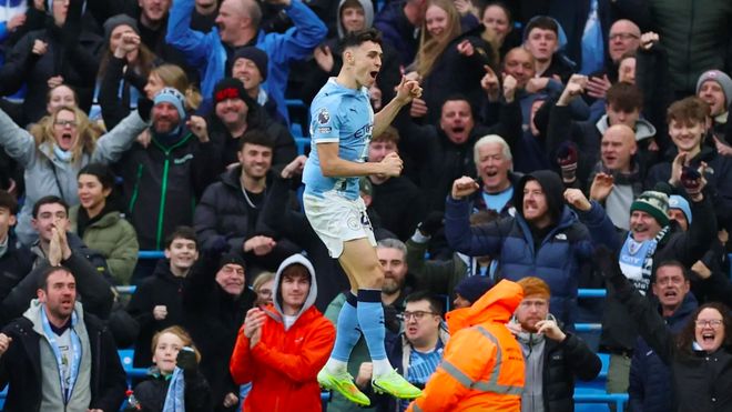 曼城球员菲尔·福登（Phil Foden）在对阵利兹联的比赛中跳起庆祝进球，背后是狂热的球迷。此图捕捉了福登在第 91 分钟绝杀利兹联、帮助曼城 3-2 险胜并终结两连败的关键时刻。