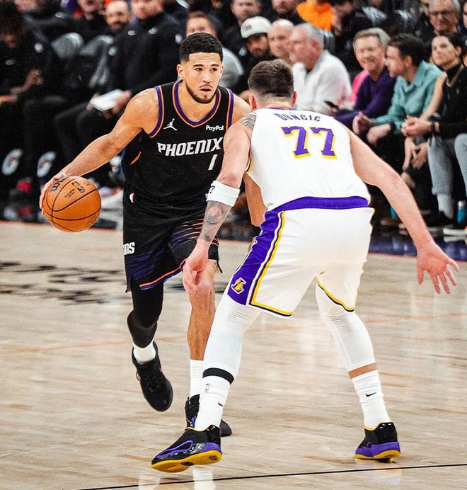菲尼克斯太阳队球星德文·布克(Devin Booker,1号)身穿黑色球衣运球,与洛杉矶湖人队球员东契奇(Luka Dončić,77号)对峙。