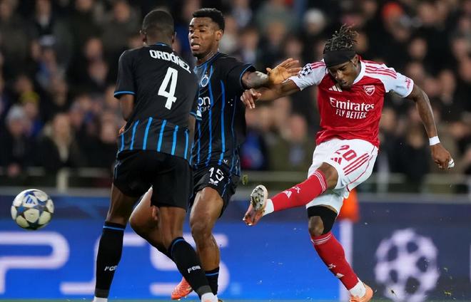 阿森納球員(紅白球衣,20號)在比賽中做出踢球或射門動作,與兩名深色球衣的對手球員進行激烈身體對抗。