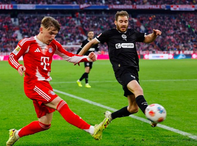 拜仁慕尼黑（红色球衣）球员在德甲联赛中与圣保利（黑色球衣）球员激烈争抢足球。此图象征拜仁在3-1 逆转圣保利的比赛中展现的竞技对抗和联赛榜首的统治力，是其狂欢夜胜利的一部分。