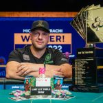 迈克尔·米兹拉奇坐于牌桌旁展示 WSOP 扑克玩家锦标赛奖杯与彩色筹码
