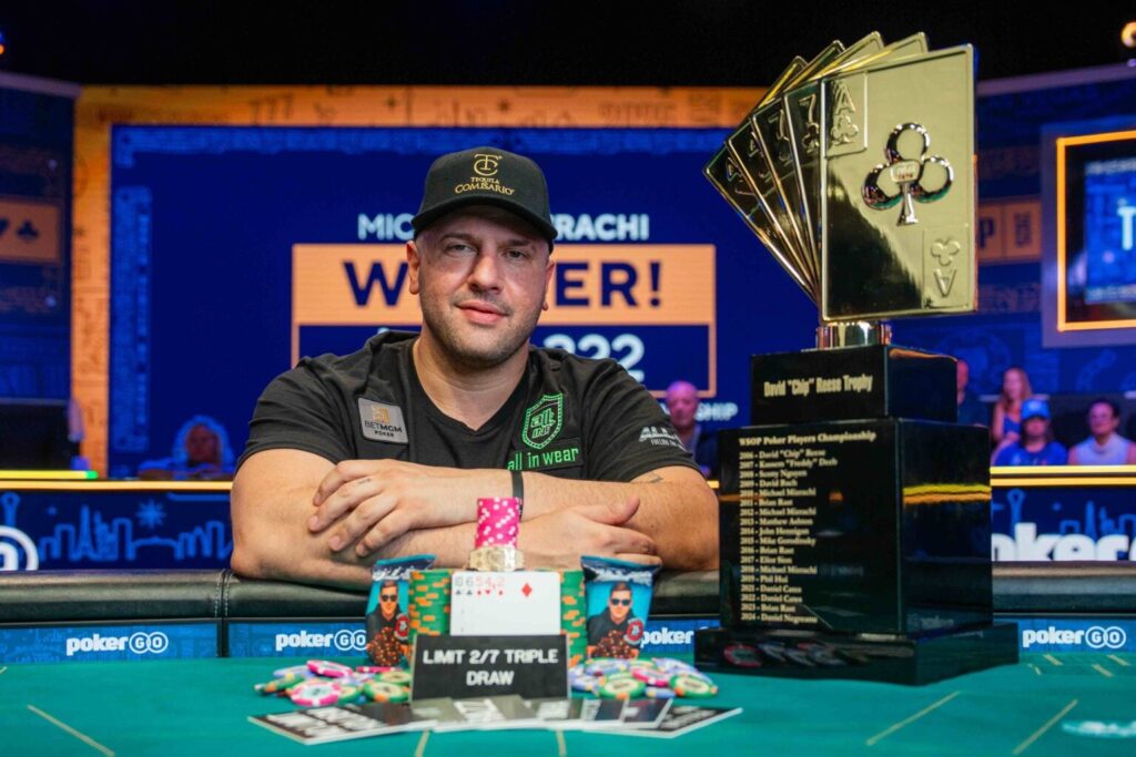 迈克尔·米兹拉奇坐于牌桌旁展示 WSOP 扑克玩家锦标赛奖杯与彩色筹码