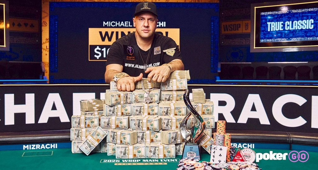 迈克尔·米兹拉奇坐在WSOP牌桌前，面前堆放大量现金、奖杯与筹码