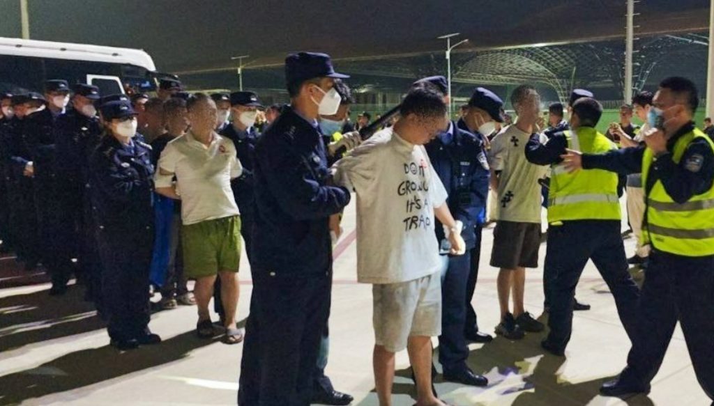 柬埔寨执法人员夜间押送涉案人员，现场有多名警察和被控制人员，反映网络诈骗打击行动