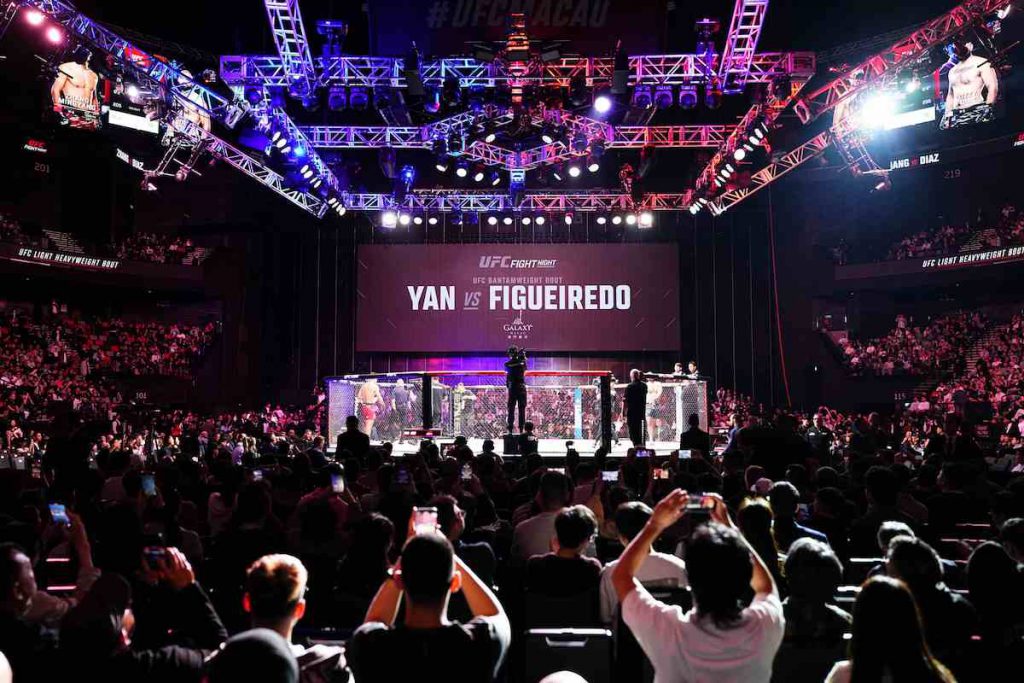 UFC格斗赛事现场观众围绕八角笼观看比赛，澳门体育娱乐活动发展受关注