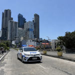 菲律宾城市道路上有警车巡逻，背景为马尼拉高楼建筑群