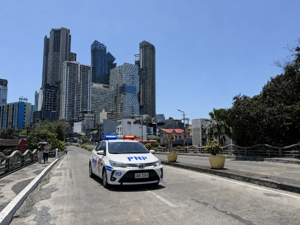 菲律宾城市道路上有警车巡逻，背景为马尼拉高楼建筑群