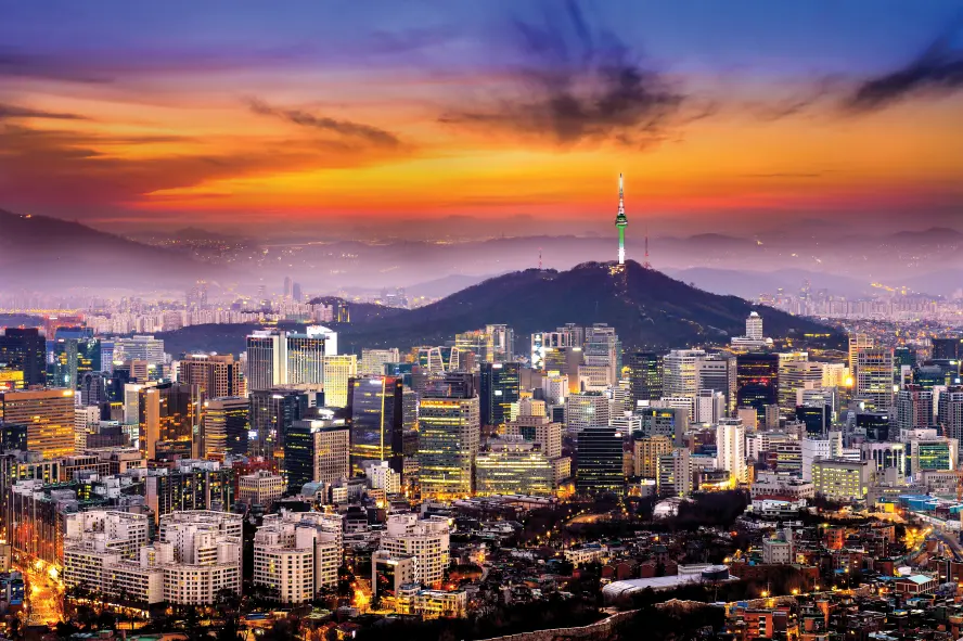 日落时分俯瞰韩国首尔城市夜景,群山之上的首尔塔在晚霞中亮起绿光,前方高楼大厦灯火通明